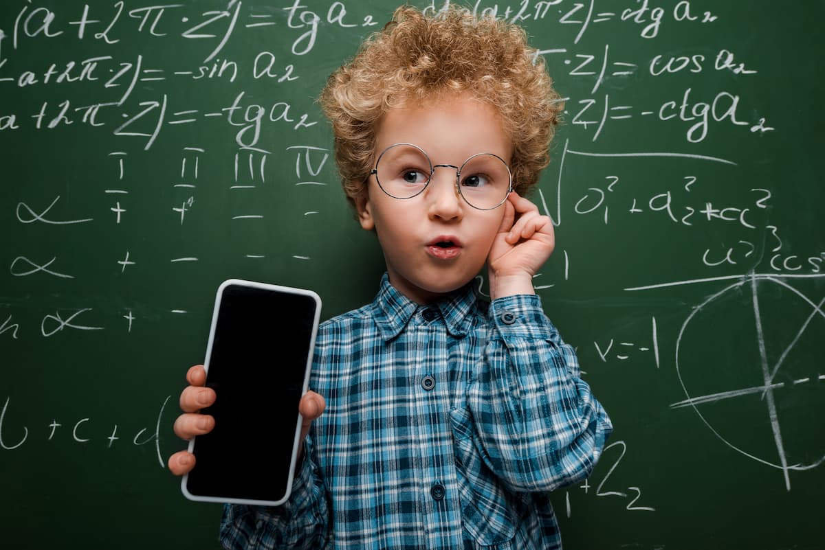 数式の書かれた黒板の近くで眼鏡に触れる賢い子供